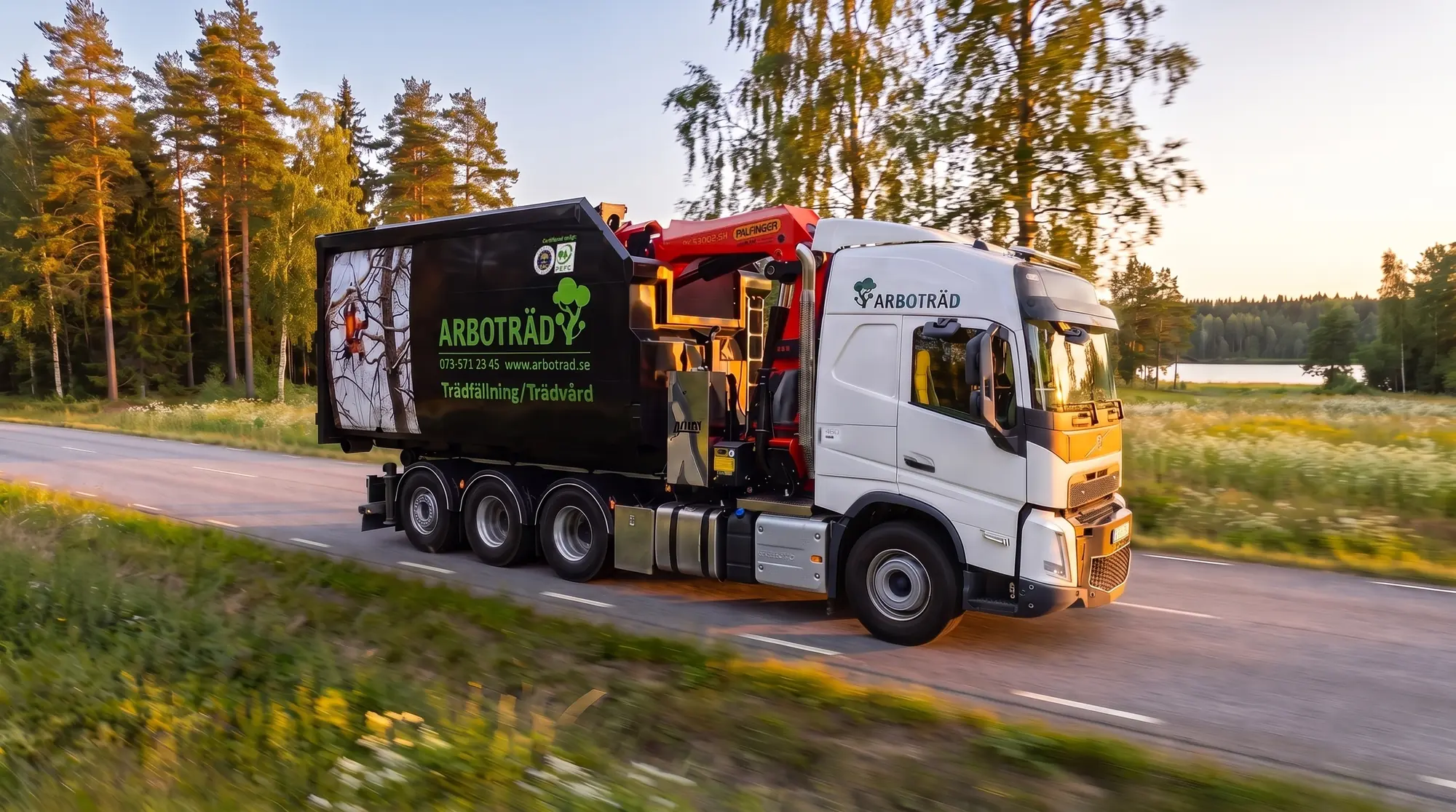 Arboträds kranbil på en landsväg genom småländsk skog i kvällsljus