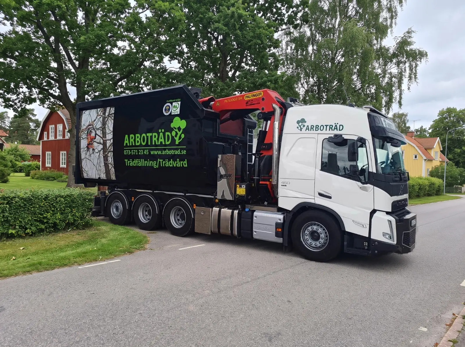 Arboträds kranbil på en villagata framför ett rött hus